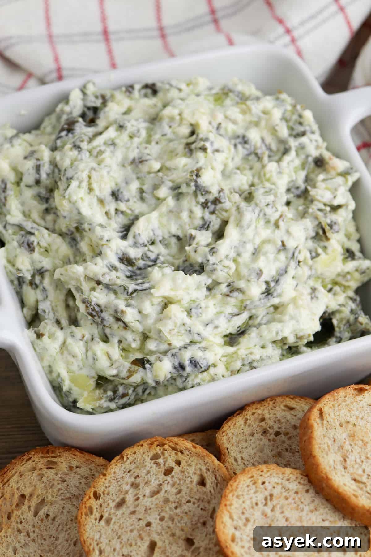 Creamy Slow Cooker Spinach and Artichoke Dip 2 creamy crockpot spinach and artichoke dip in white bowl served with small pieces of bread for dipping