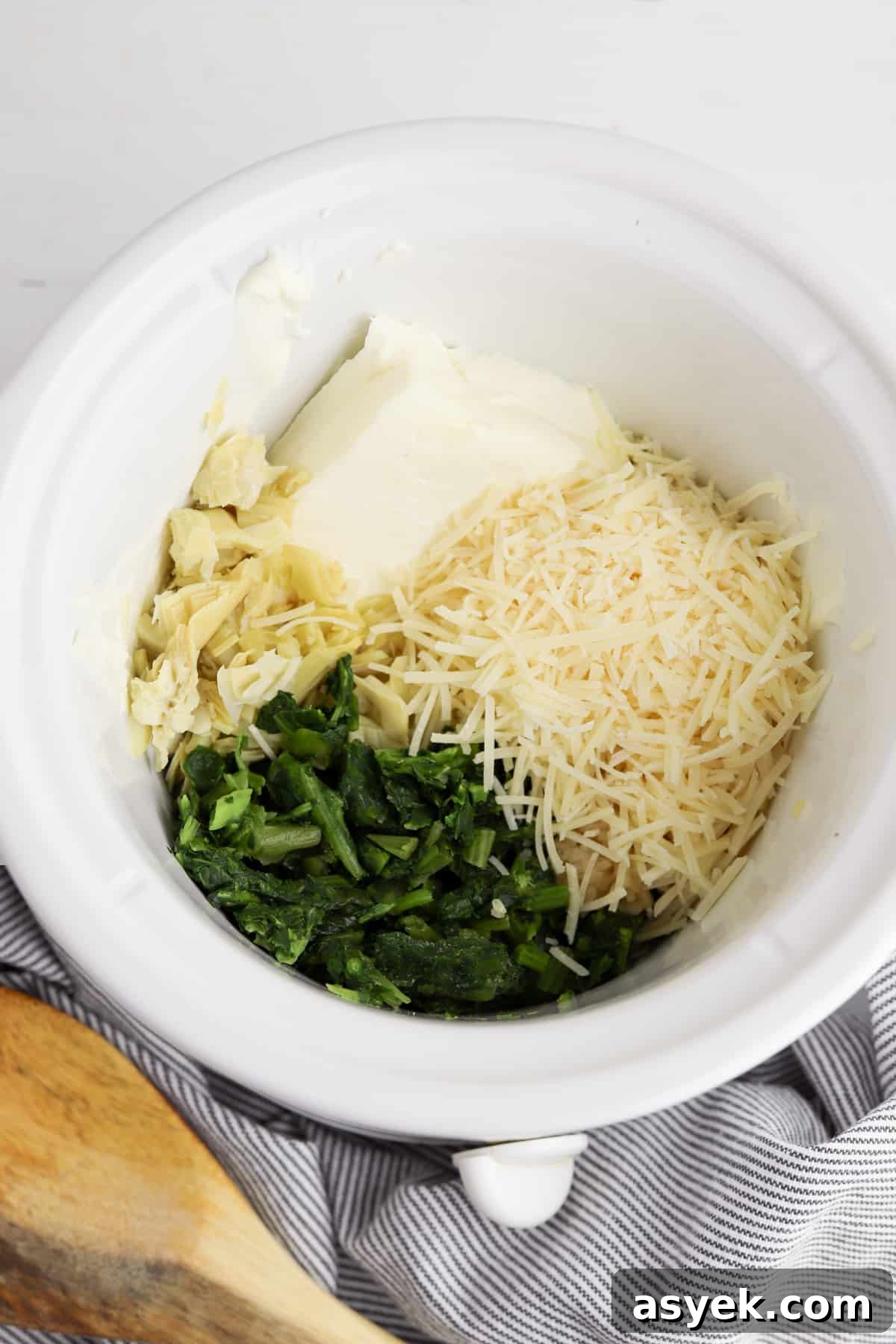 Creamy Slow Cooker Spinach and Artichoke Dip 3 Cream cheese, spinach, artichokes, garlic, and shredded cheese in round white crockpot
