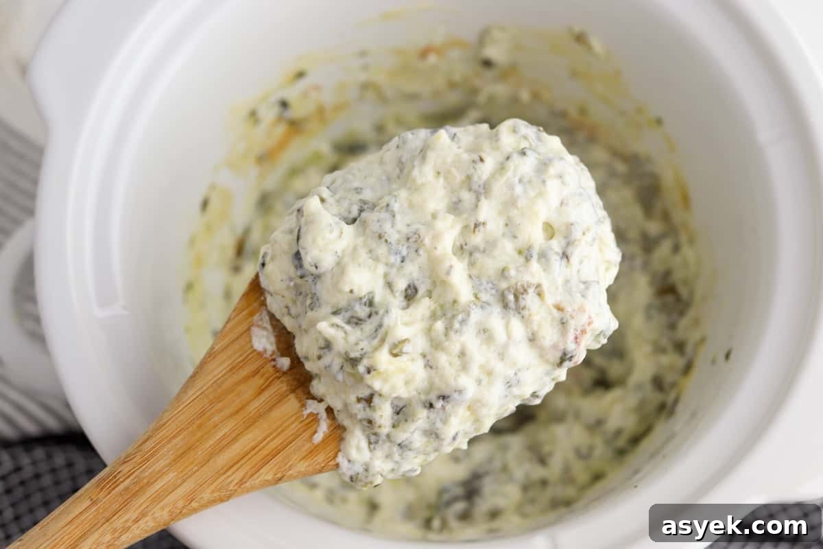 Creamy Slow Cooker Spinach and Artichoke Dip 5 crockpot spinach artichoke dip with a wooden spoon scooping some of the dip out