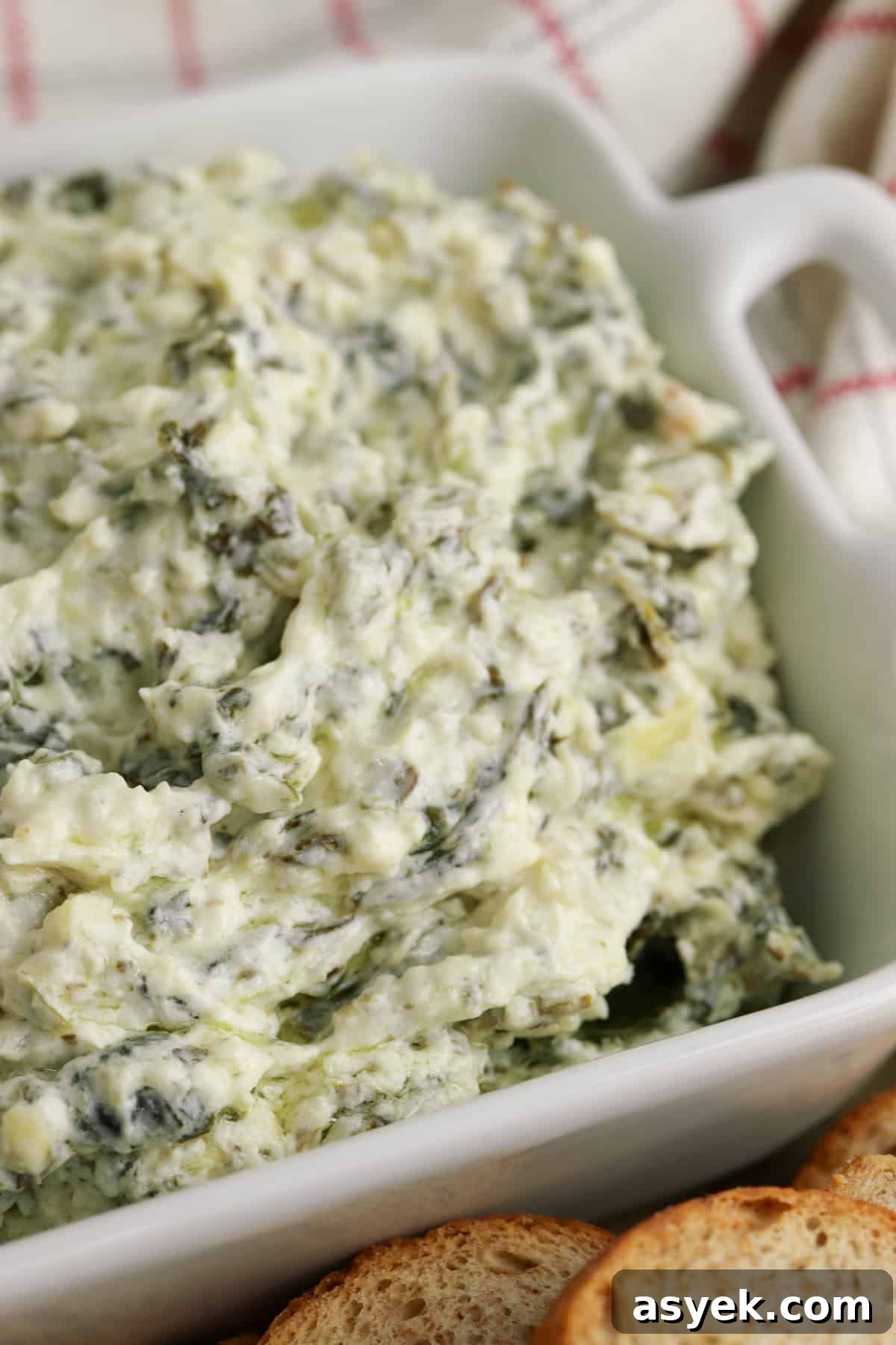 Creamy Slow Cooker Spinach and Artichoke Dip 6 Creamy and cheesy slow cooker spinach artichoke dip in white serving bowl with small pieces of bread for dipping
