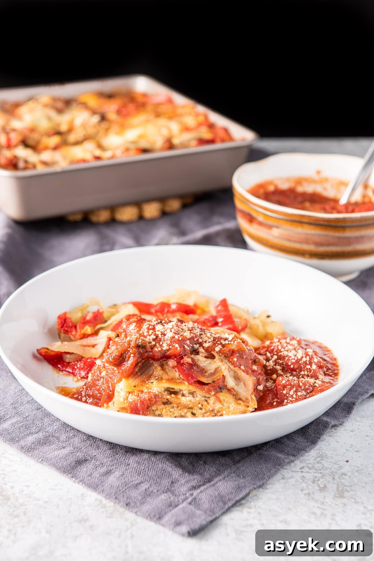 A white plate with lasagna on it with the pan of it behind