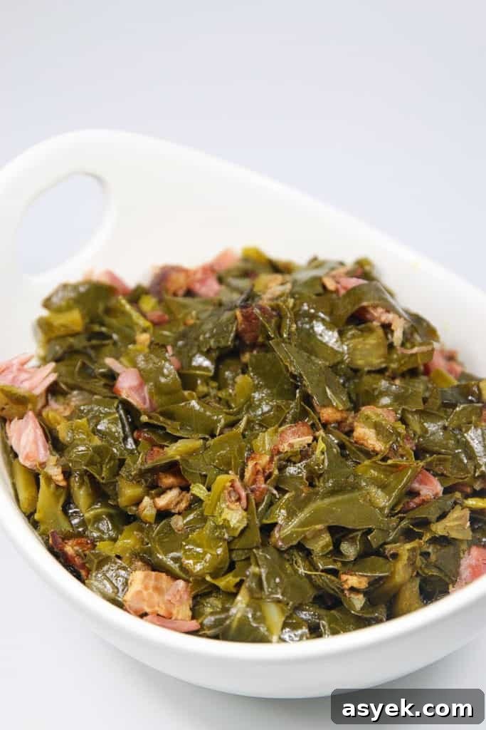 a white bowl of cooked collard greens with chunks of ham pieces