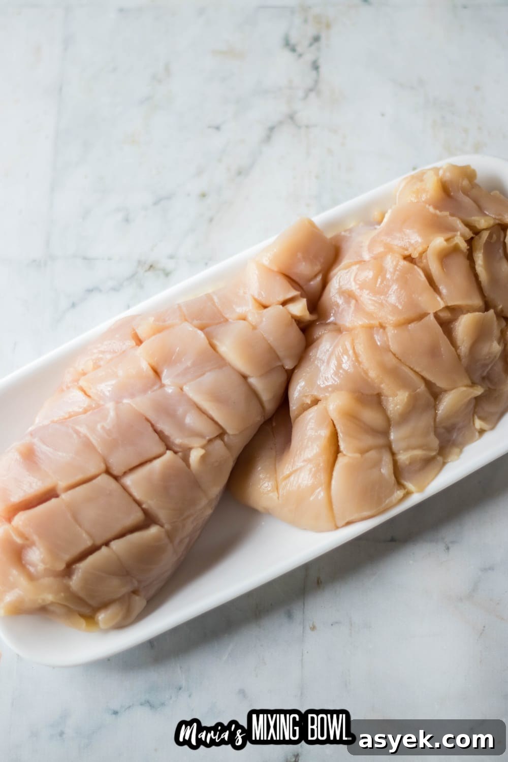 raw chicken breasts scored on a white plate