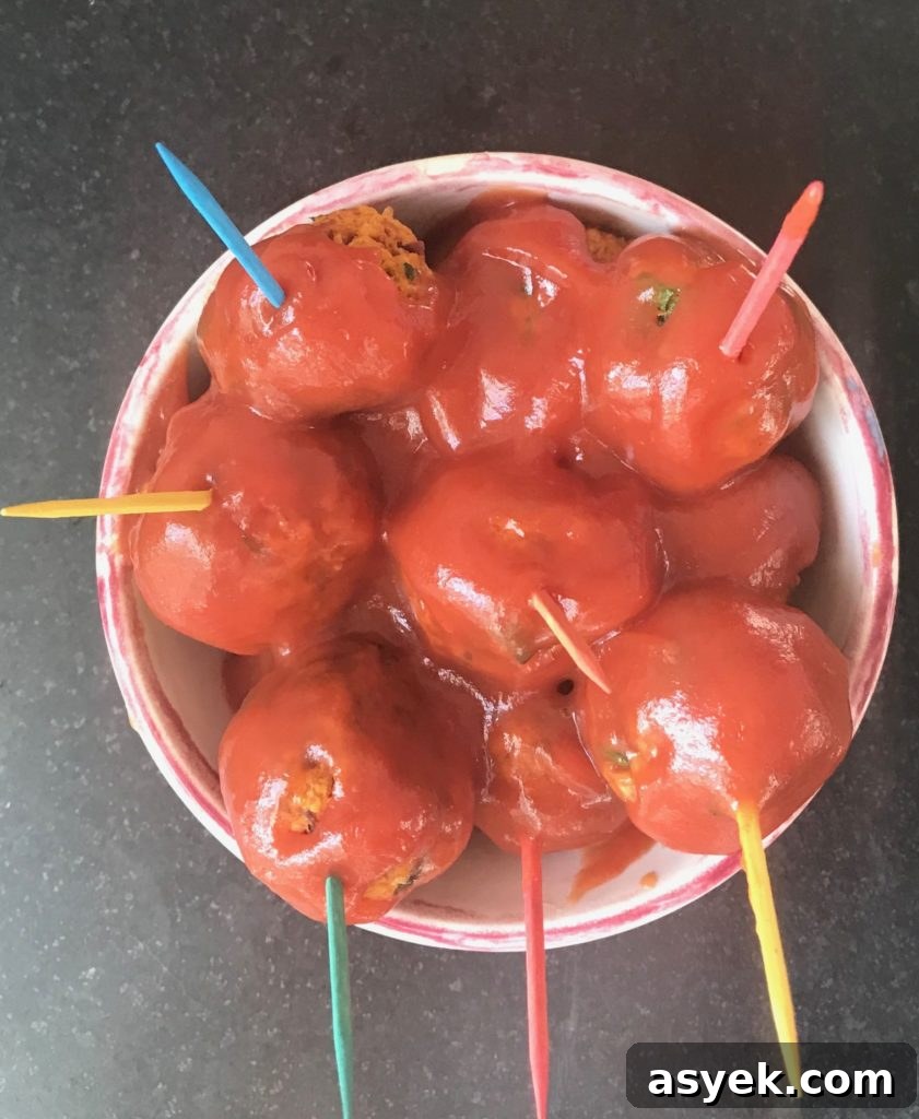 Small dish filled with vegan meatballs in a bright red sweet and sour sauce. Meatballs have brightly colored toothpicks in them.