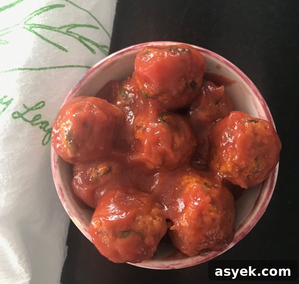 Vegan Meatballs in a sweet and sour sauce. Appetizer size in a small bowl with a white tea towel/green design on the side.