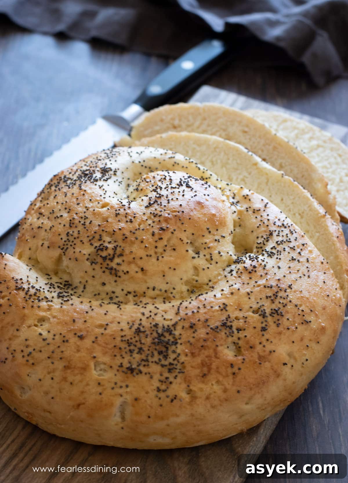 A round gluten free challah on a wooden cutting board.