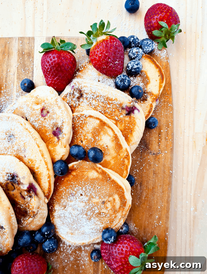 Pancakes sprinkled with icing sugar on a wooden board, decorated with blueberries and strawberries