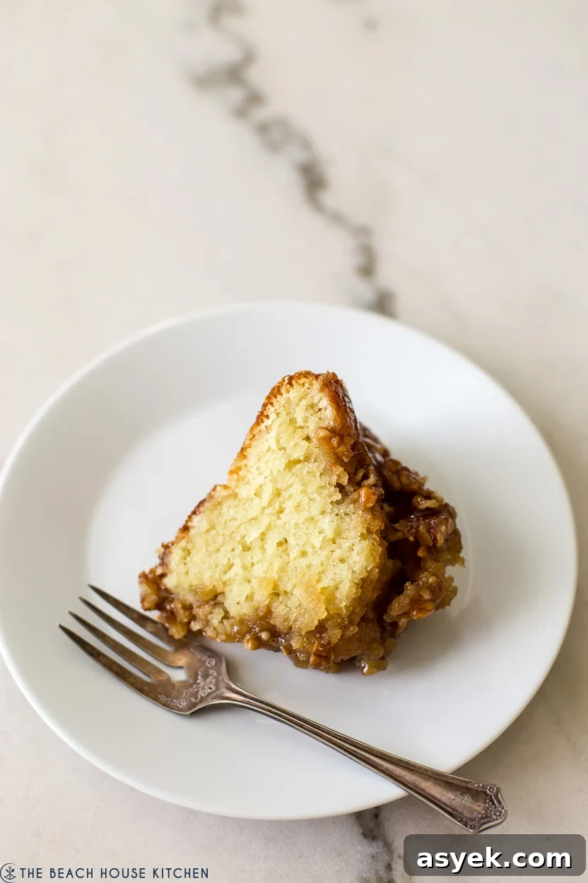 Classic Pecan Pie Bundt Cake Recipe 7 A slice of a pecan topped cake on a white plate with a fork