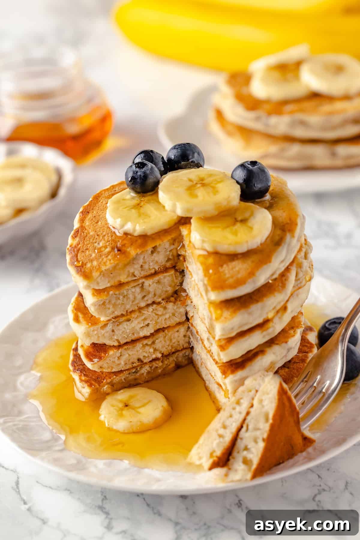 Stack of vegan banana pancakes on plate with syrup and fruit