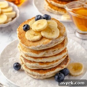 Stack of fluffy banana pancakes on plate with fresh fruit
