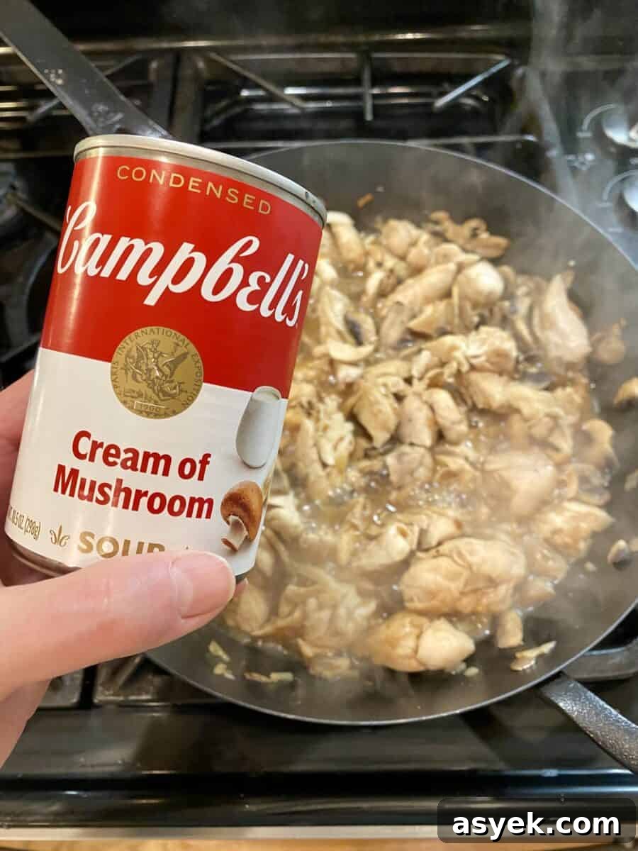 A can of cream of mushroom held over a pan of sauce.
