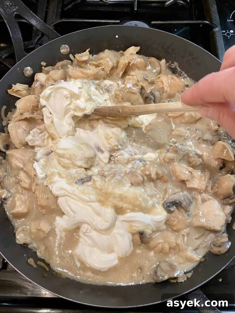 Stirring sour cream into the chicken stroganoff mixture in a skillet