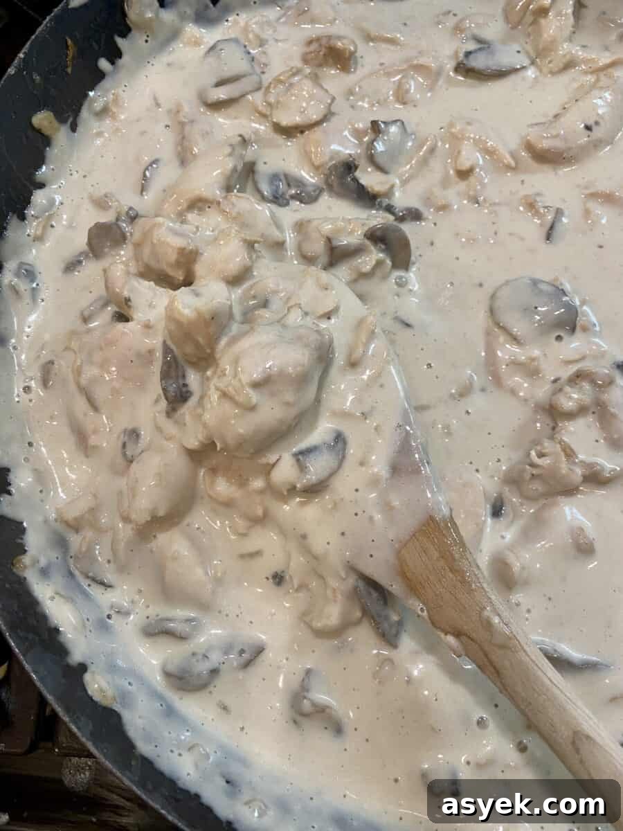 Stroganoff cooking in a skillet on the stove with a wooden spoon stirring the contents