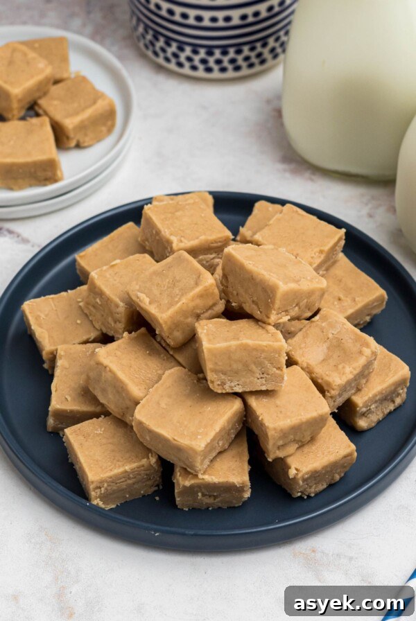 Creamy fudge, cut into small pieces, stacked on a blue plate, in front of jars of milk.