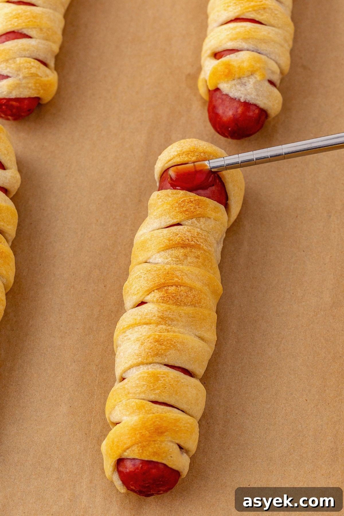 Halloween Mummy Hot Dogs Recipe 7 Ketchup being added to mummy dog to use to hold candy eyes in place.