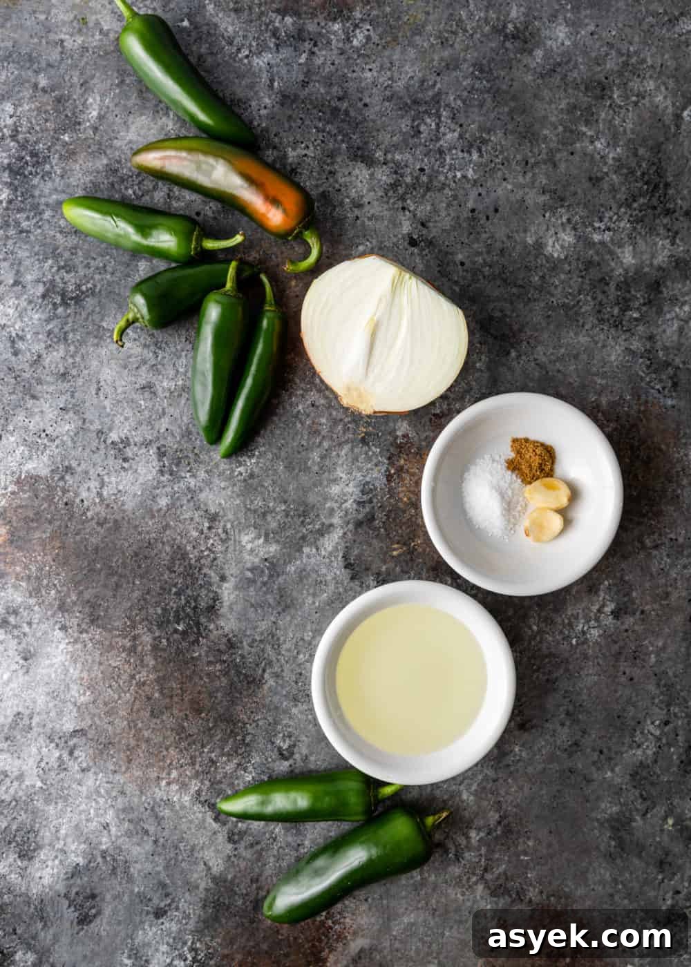 overhead image: whole jalapenos, half of white onion and bowl of spices to make spicy Mexican dip