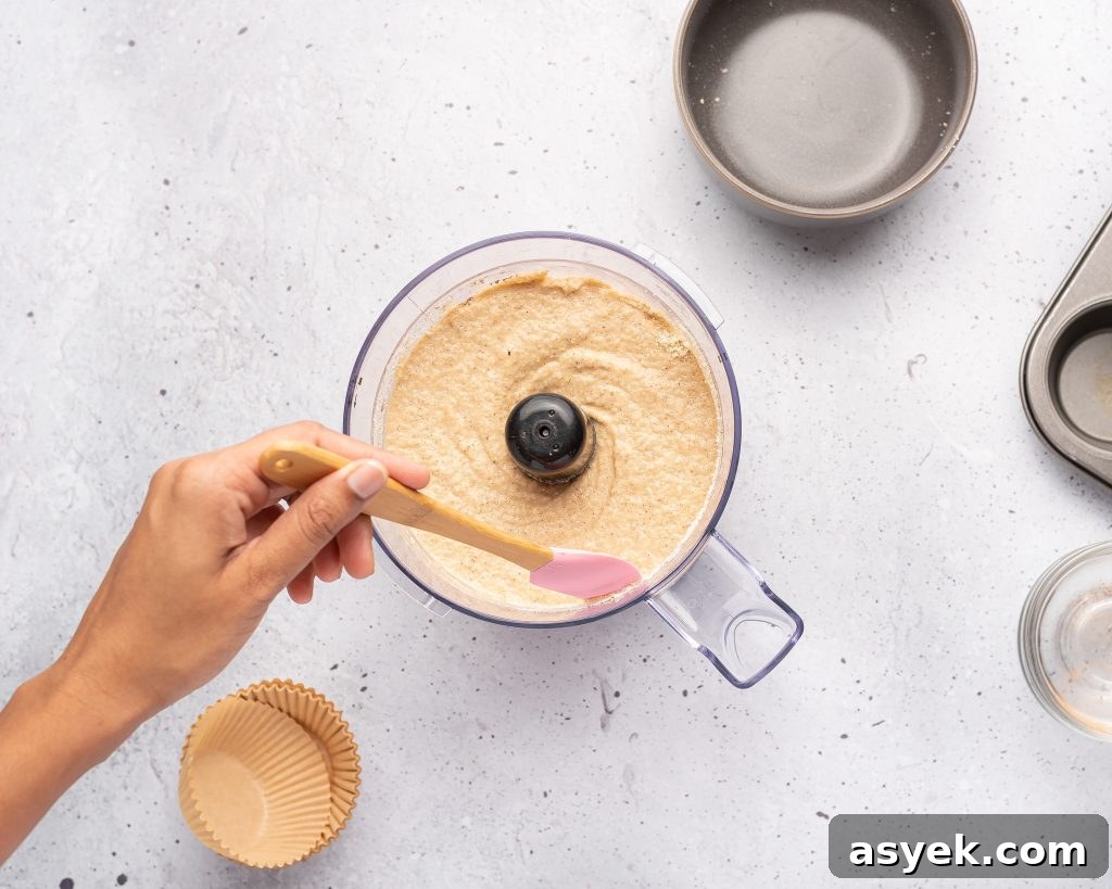 High-Protein Almond Flour Banana Muffins: Gluten-Free Snacks 4 scraping down the sides of a food processor with muffin batter inside with a spatula