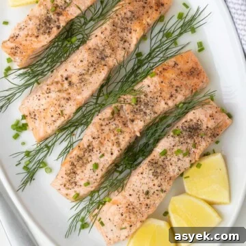 Close up of a platter of salmon filets with lemon and herbs on a table.