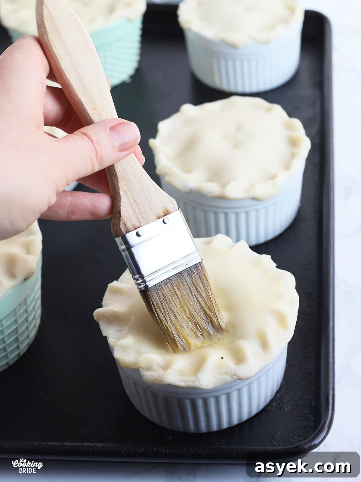 hand using a pastry brush to apply egg wash to the crust of a mini pot pie