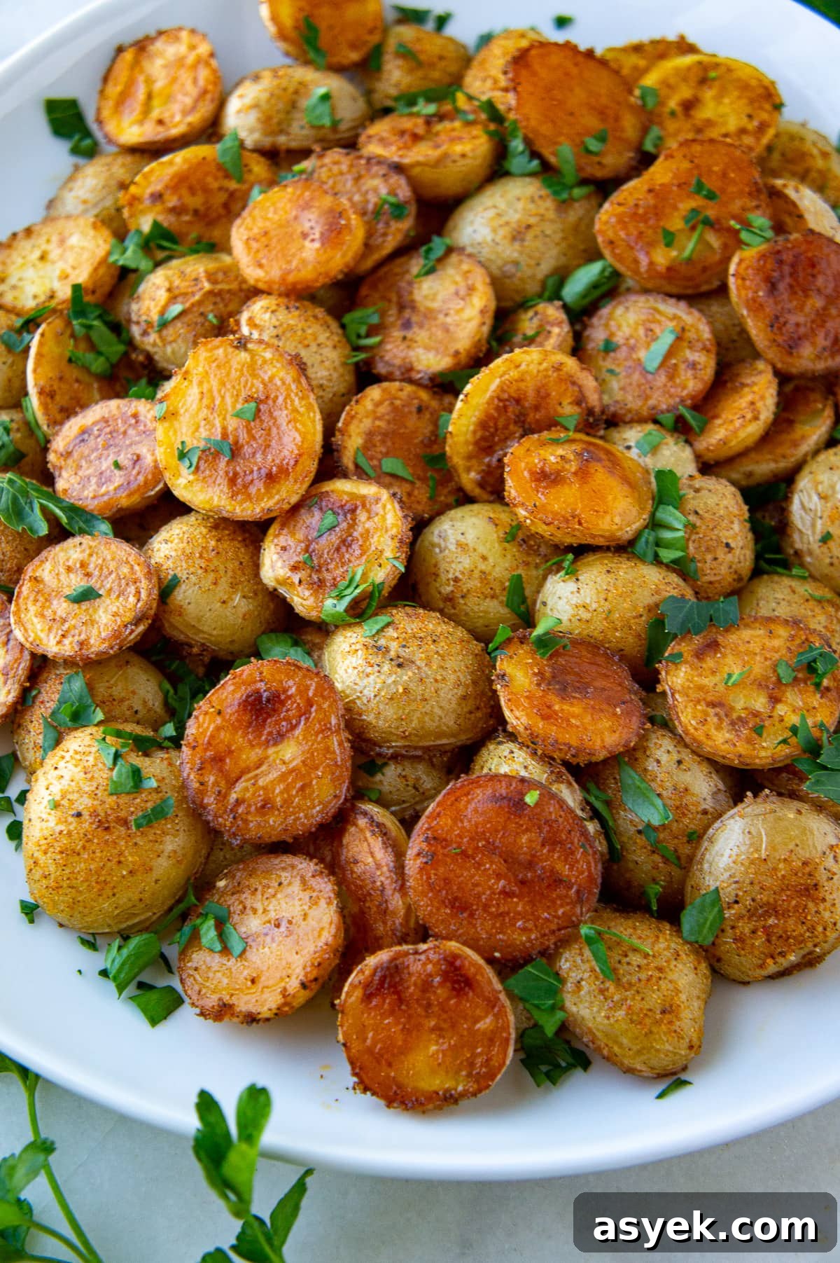 golden brown baby potatoes on a white platter with chopped parsley.