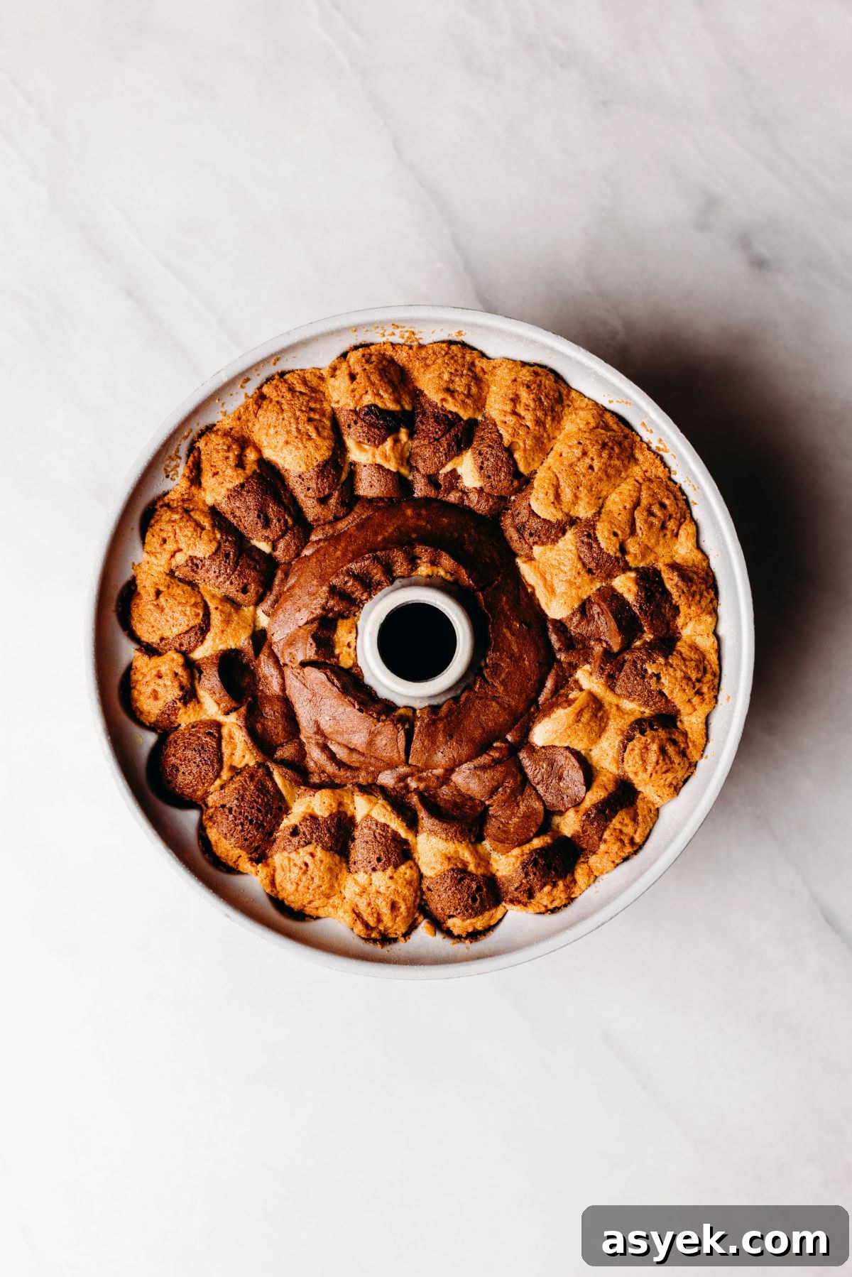 Classic Marble Bundt Cake Recipe with Chocolate Swirls 11 Baked marble bundt cake in a bundt cake pan on a white marbled background.