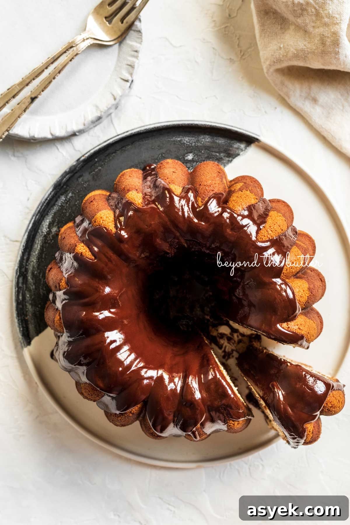 Classic Marble Bundt Cake Recipe with Chocolate Swirls 15 Marble bundt cake on a black and white ceramic dessert plate with chocolate ganache glaze drizzled over the top with a a slice partially removed.