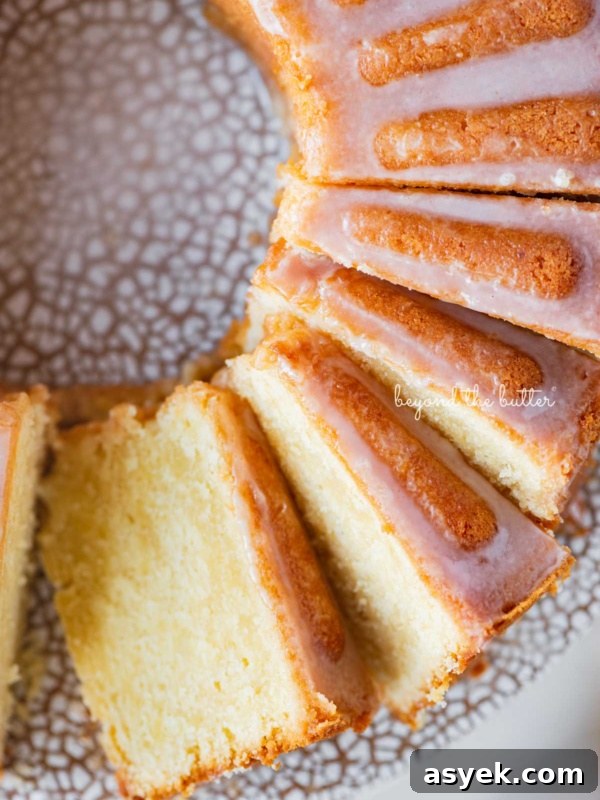 Sliced lemon cream cheese pound cake with a lemon glaze on a ceramic cake stand.