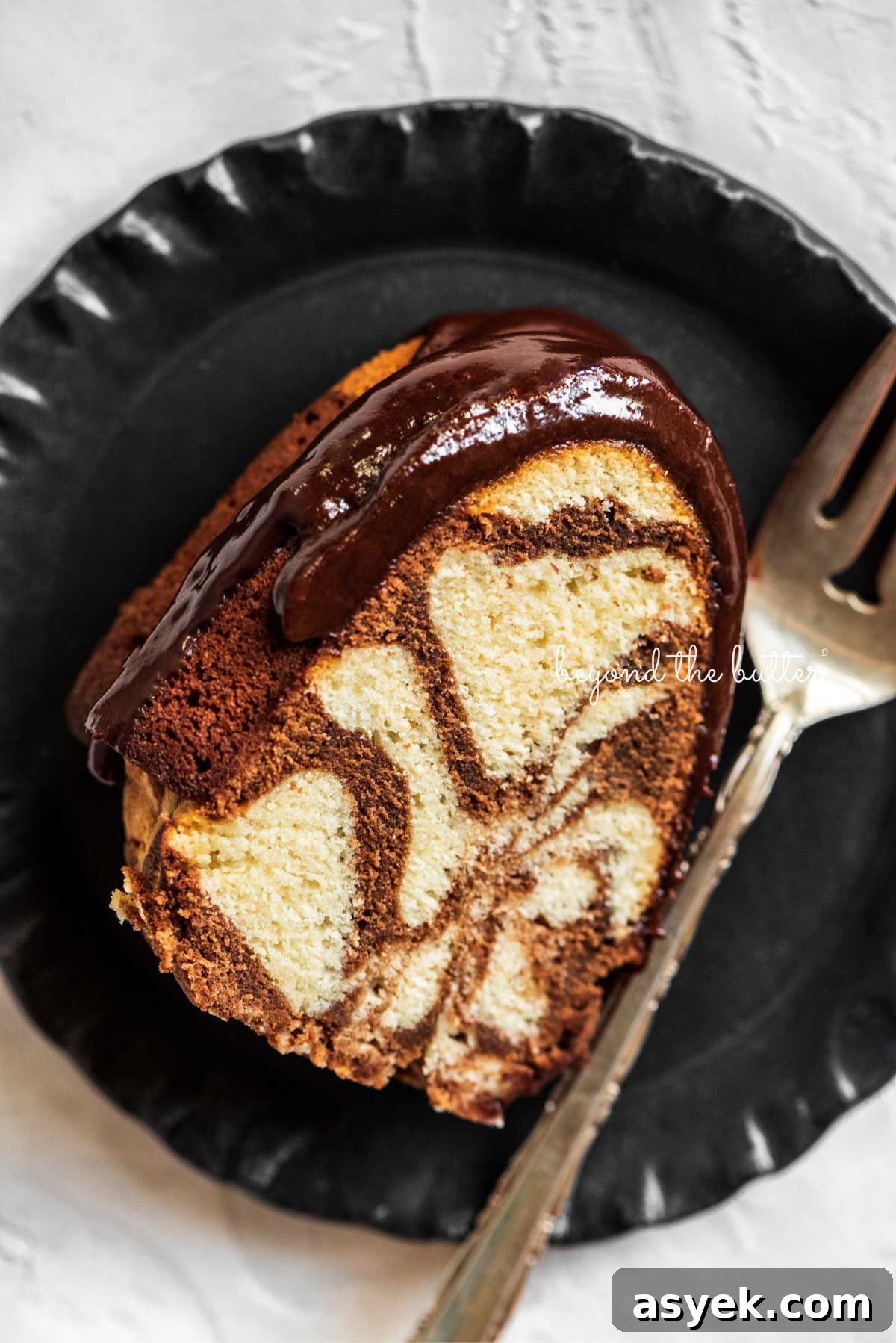 Classic Marble Bundt Cake Recipe with Chocolate Swirls 3 Slice of marble bundt cake on black dessert plate with fork placed next to it on a white background.