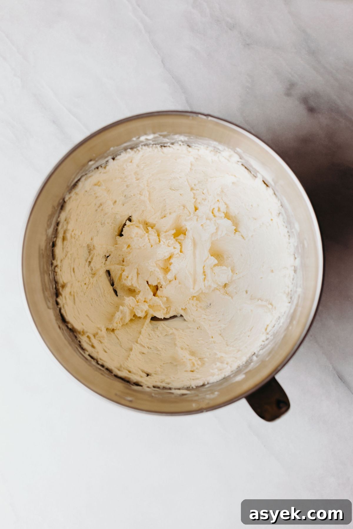 Classic Marble Bundt Cake Recipe with Chocolate Swirls 5 Beaten cream cheese and unsalted butter in a stainless steel mixing bowl on a white marbled background.