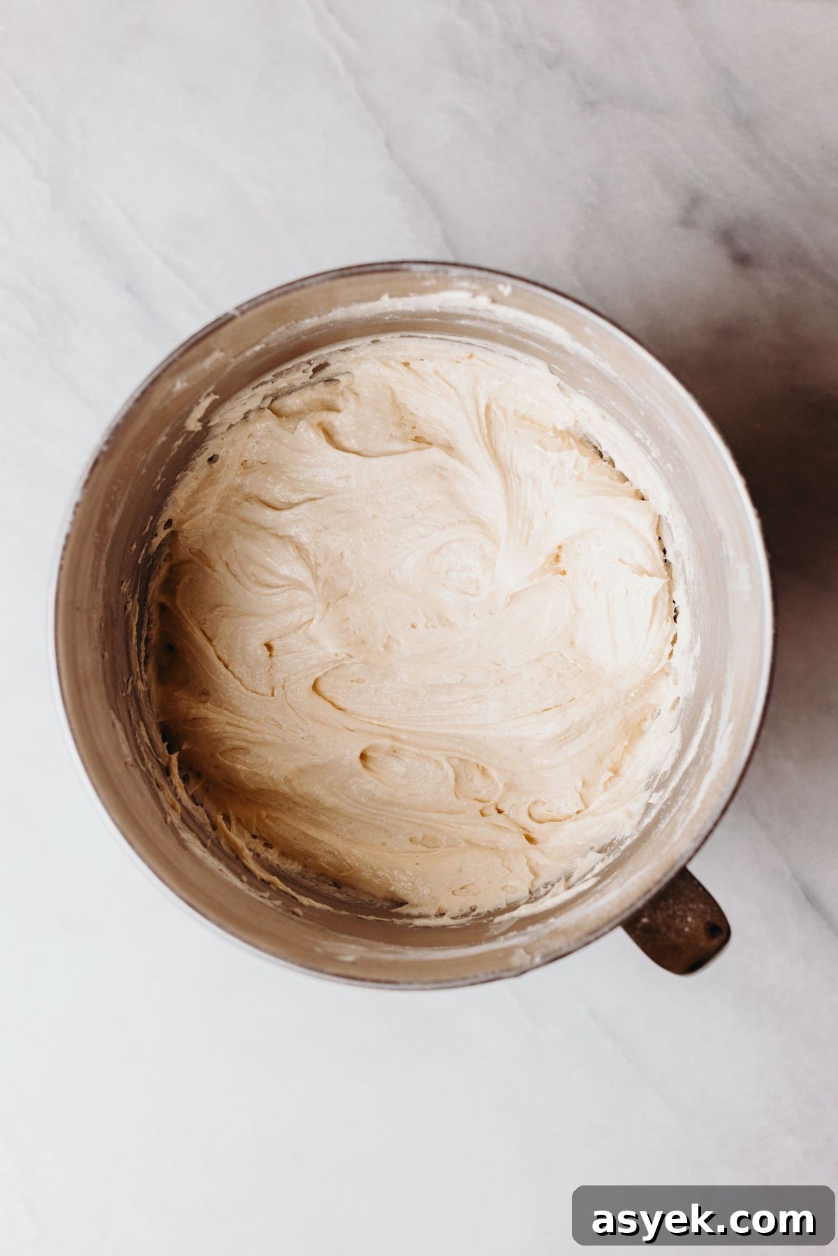 Classic Marble Bundt Cake Recipe with Chocolate Swirls 7 Bundt cake batter after adding the eggs and flour in a stainless steel mixing bowl on a white marbled background.