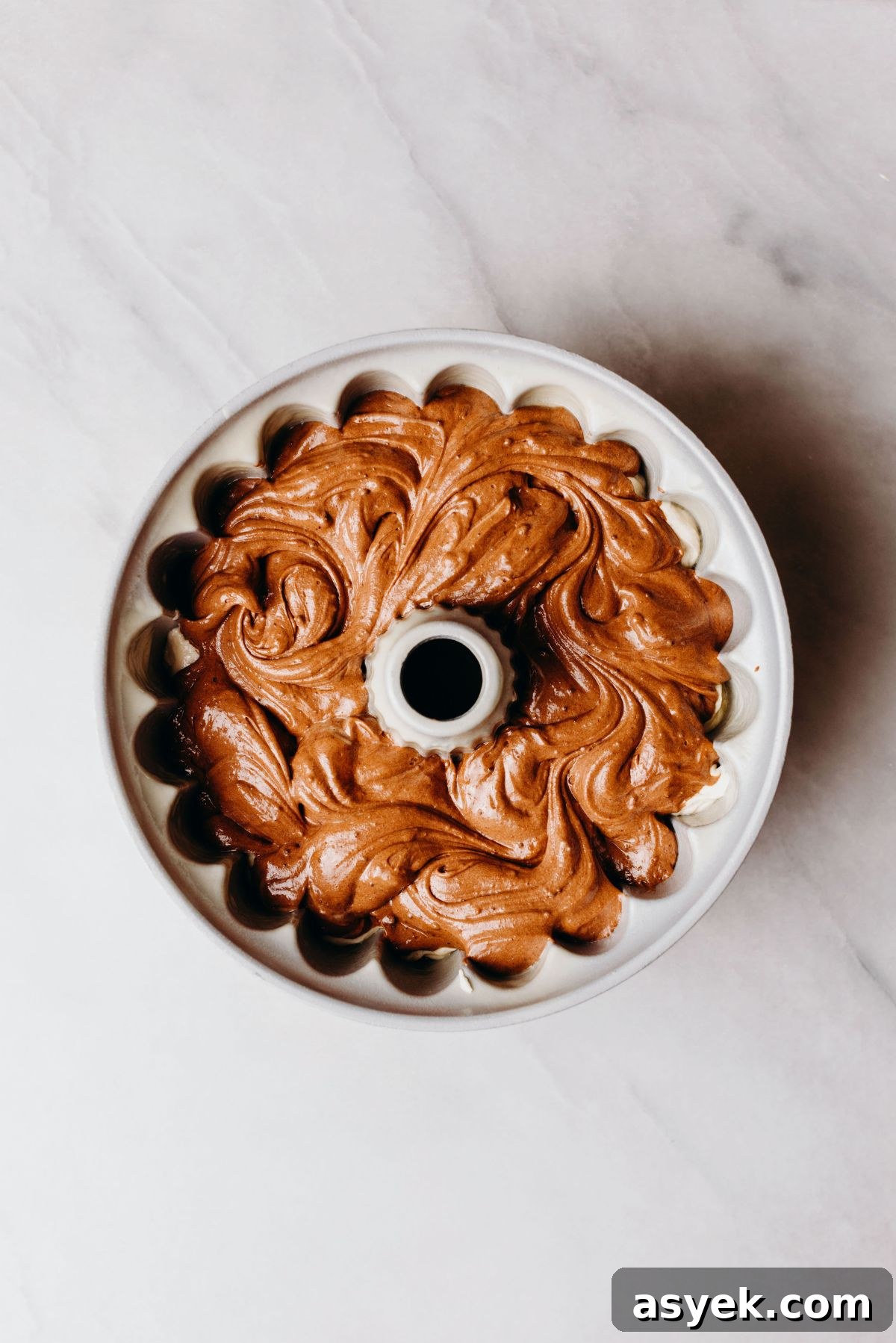 Classic Marble Bundt Cake Recipe with Chocolate Swirls 10 Swirled chocolate and vanilla cake batter in a bundt cake pan on a white marbled background.
