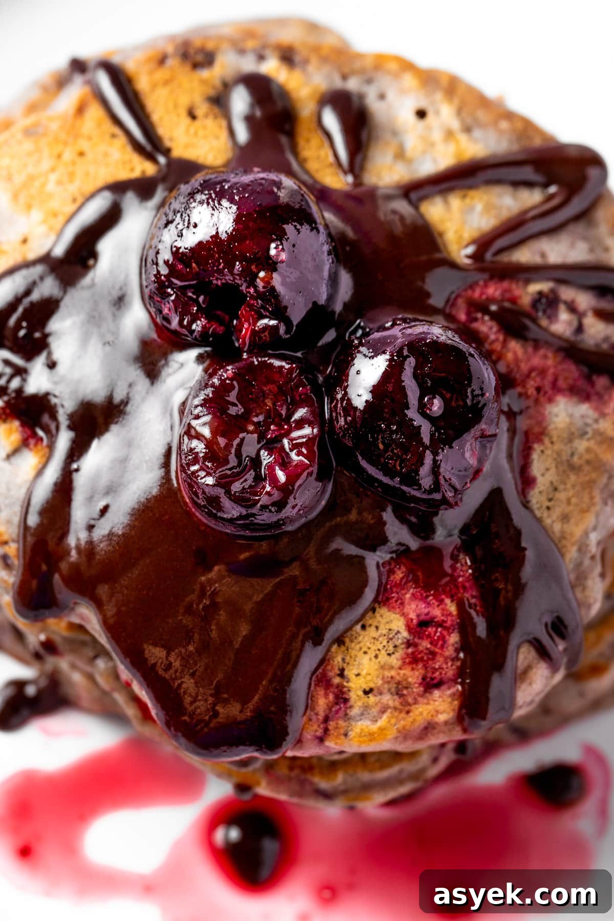 Fluffy Cherry Pancakes with Maple Syrup 2 Cherry pancakes topped with chocolate sauce, cherry sauce and three round cherries.