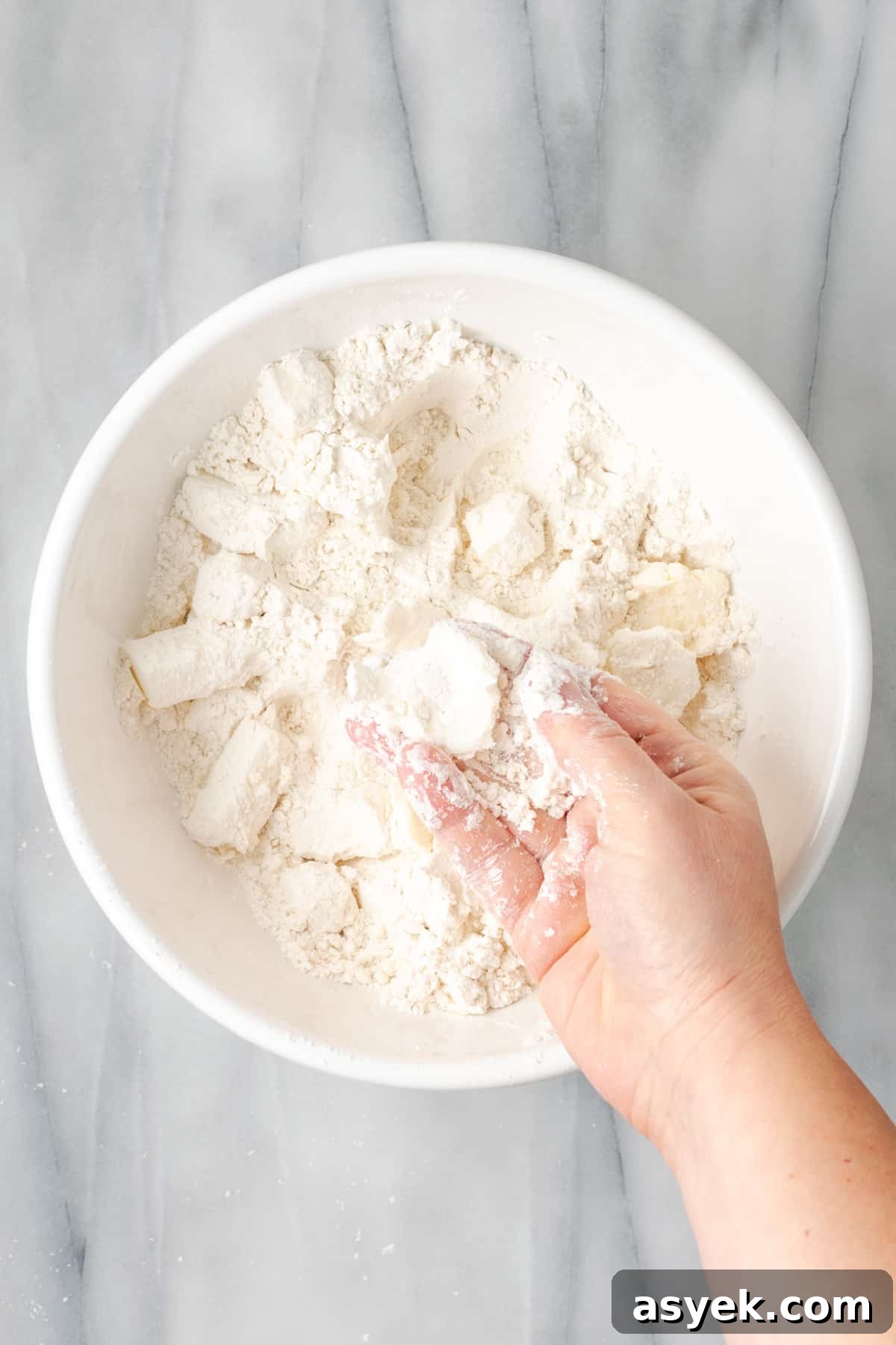 A hand squishing cubes of butter into flattened discs.