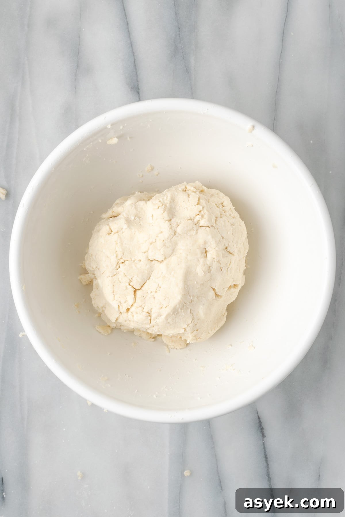 Gluten free pie dough formed into a large ball in a white mixing bowl.