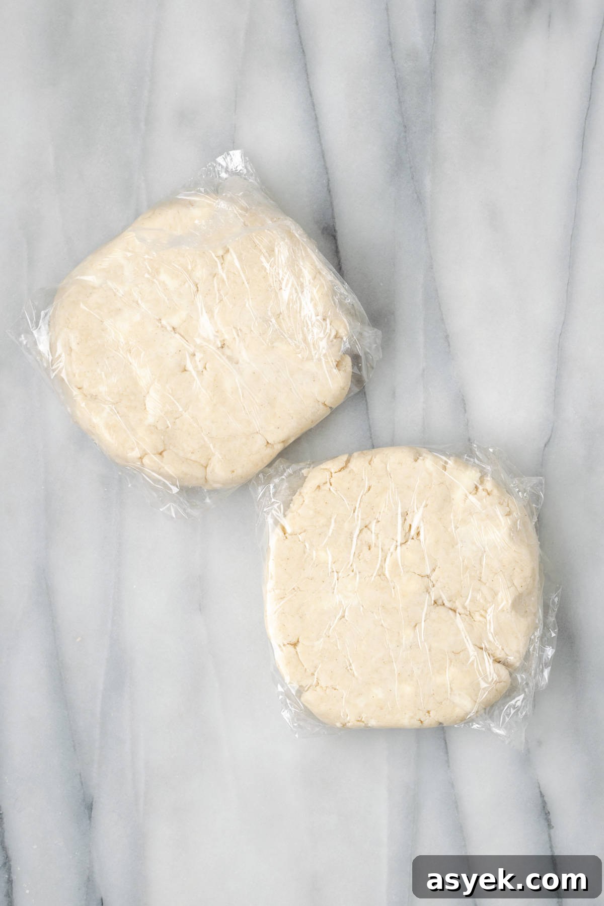 Two portions of gluten free pie crust wrapped in plastic wrap.