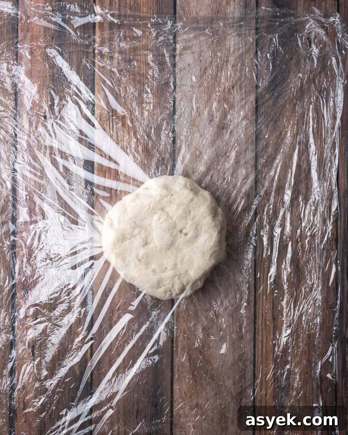 A circle of pie dough in between two sheets of plastic wrap.
