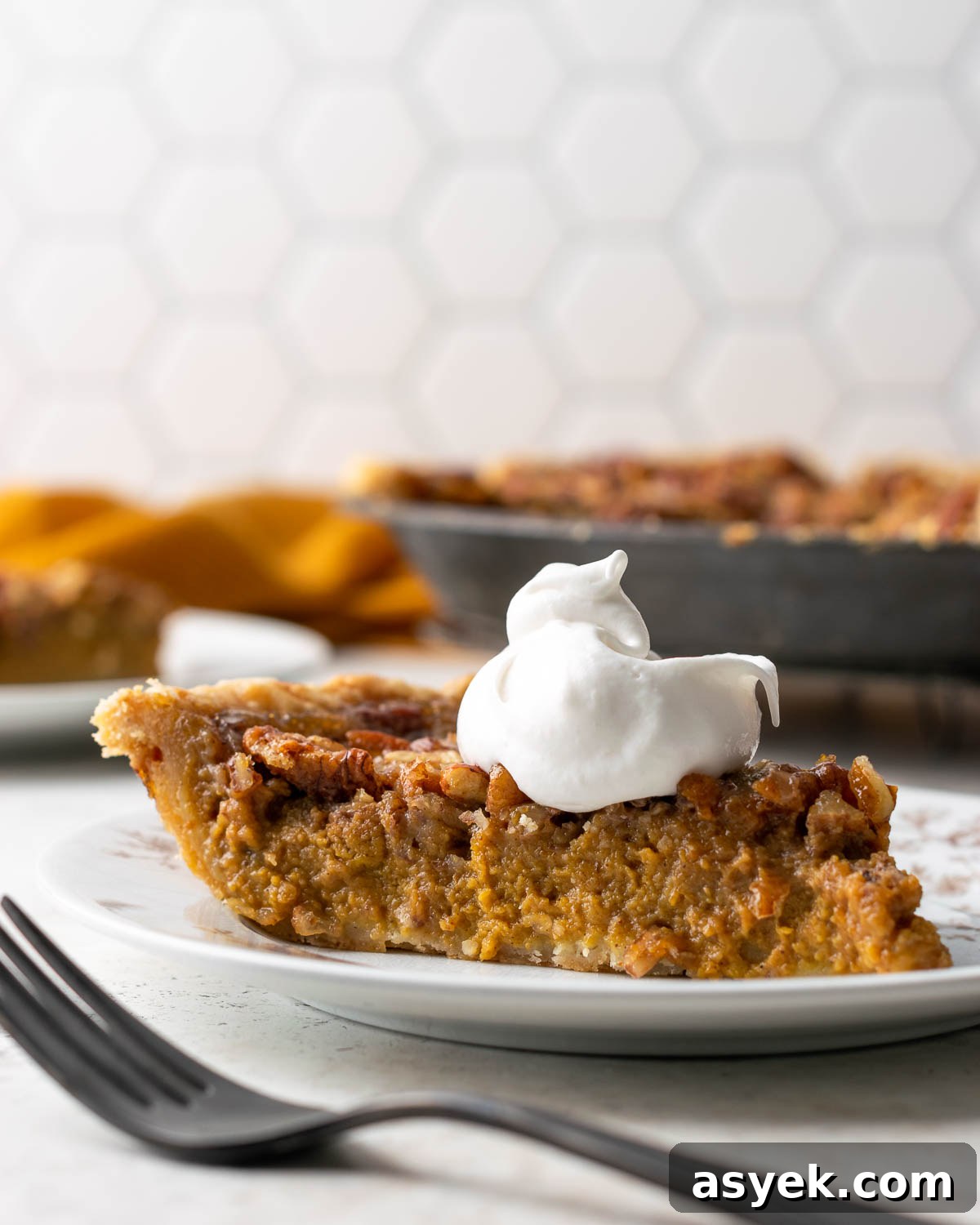 A slice of gluten free pumpkin pecan pie topped with whipped cream.