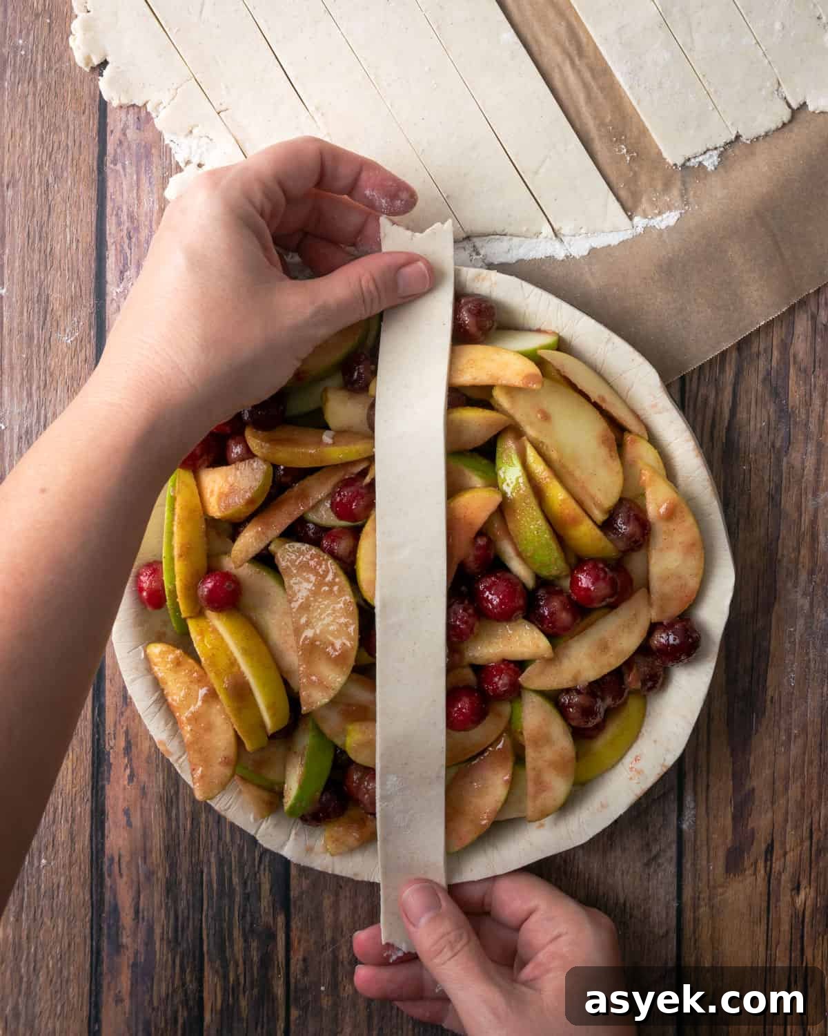 A strip of pie dough being placed over the top of an unbaked apple cranberry pie.