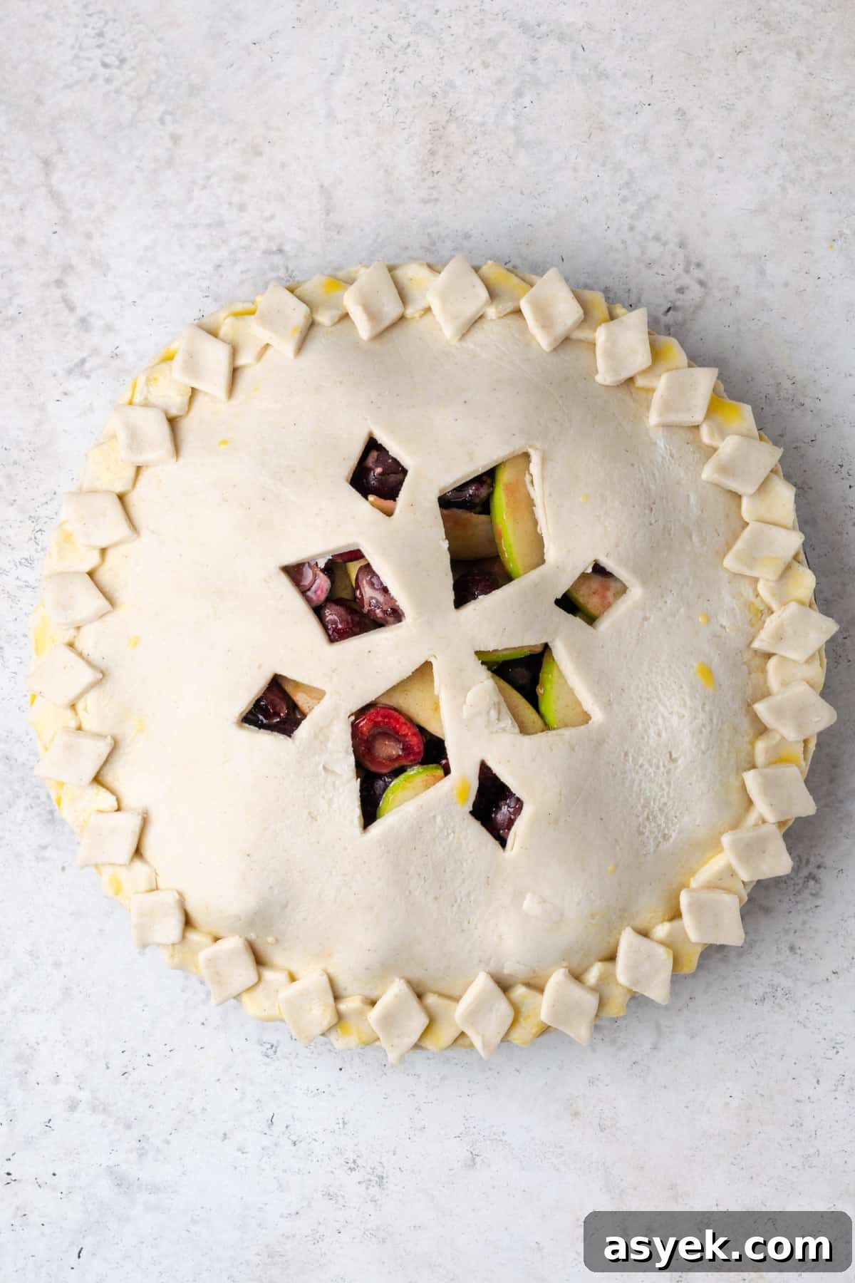 An unbaked pie with a decorative crust made of diamond shapes cut out and placed around the edge of the crust.