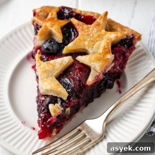 A slice of strawberry blueberry pie topped with star shaped pie crust on a white plate.