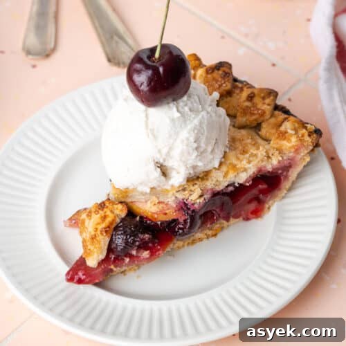 A slice of apple cherry pie topped with vanilla ice cream.