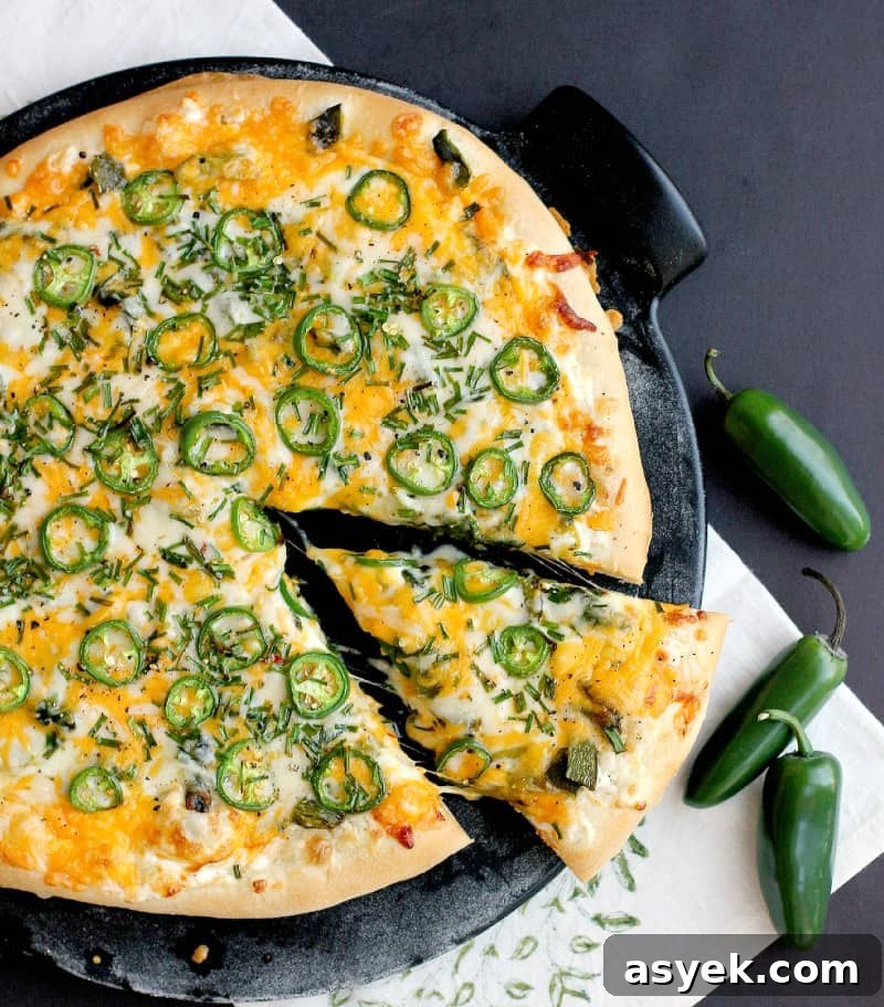 Jalapeno Popper Pizza Recipe with Cream Cheese Filling 3 top view of the finished jalapeno popper pizza on a black pizza stone with a black background. a single slice is cut in the pizza and pulled out a bit.