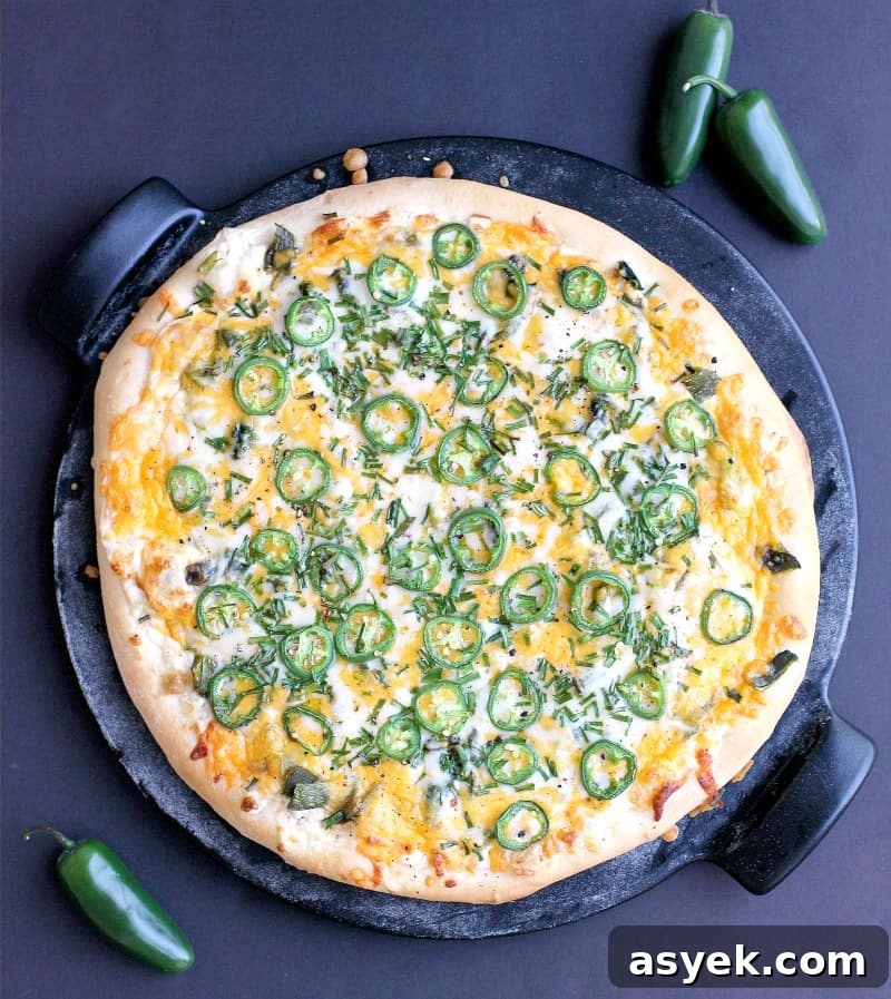 Jalapeno Popper Pizza Recipe with Cream Cheese Filling 8 top down view of the finished pizza on the pizza stone with a black background. a couple jalapenos are scattered around