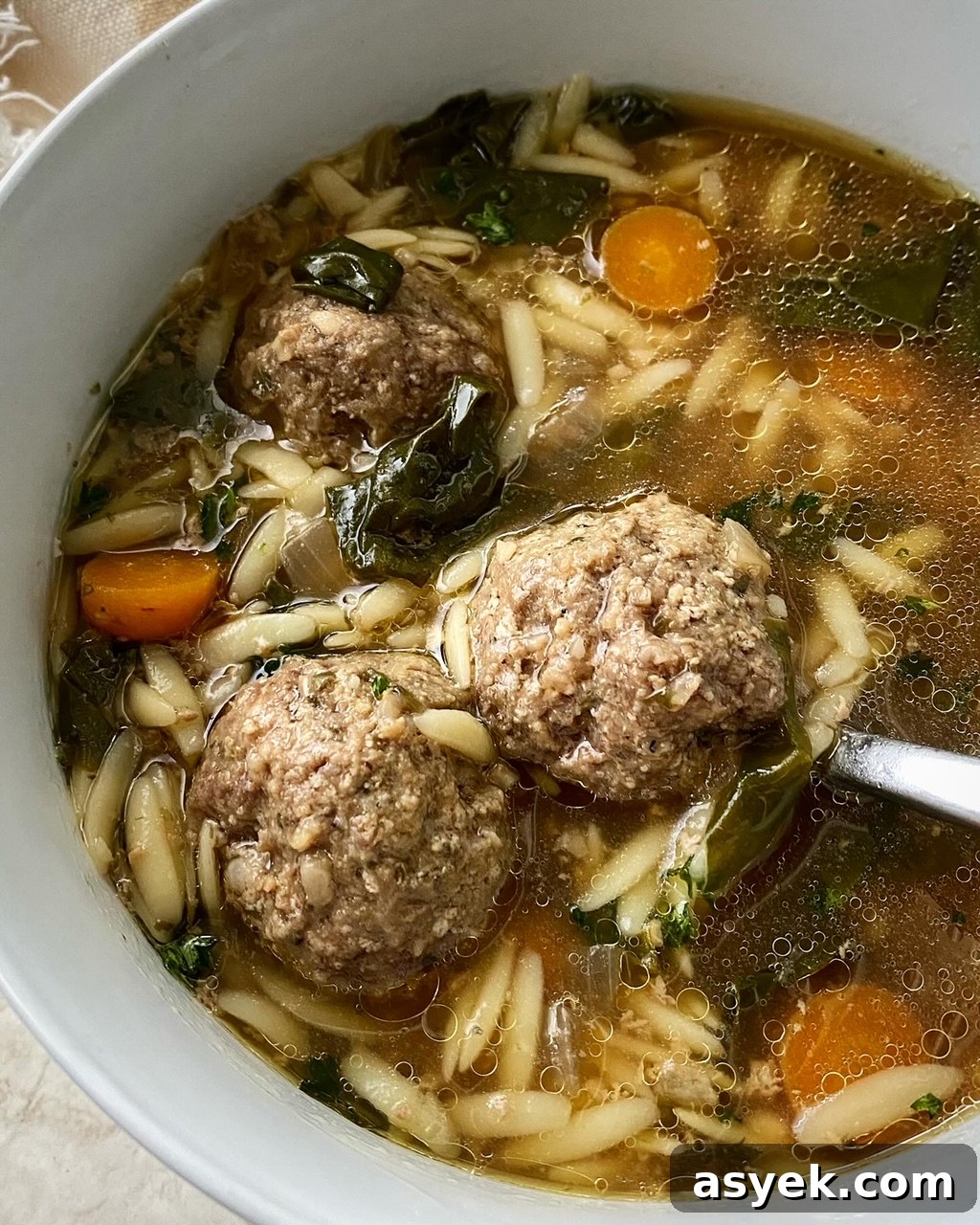 close up shot of Italian wedding soup in a white bowl with a silver spoon