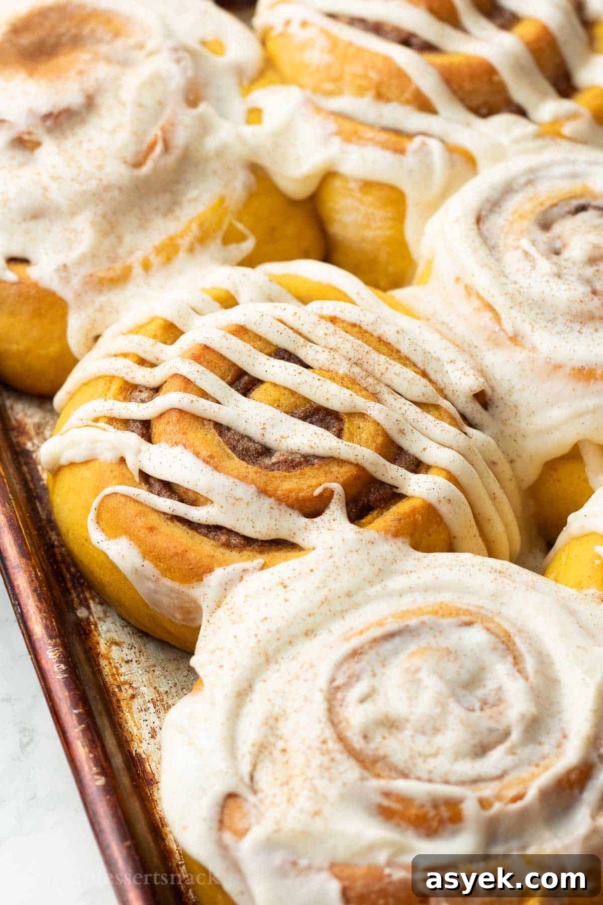Homemade Pumpkin Cinnamon Rolls with Maple Glaze 2 Baked frosted pumpkin cinnamon rolls in metal pan.