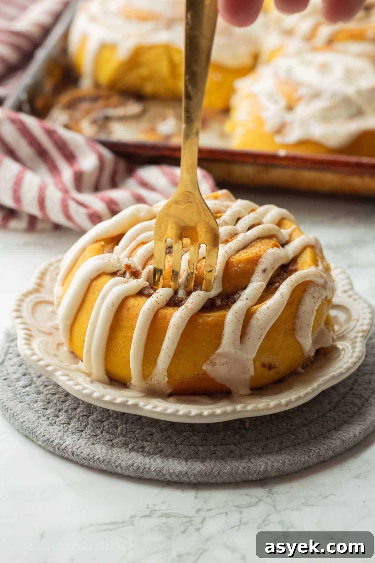 Homemade Pumpkin Cinnamon Rolls with Maple Glaze 12 Gold fork in iced pumpkin cinnamon roll on white plate.