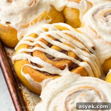 Homemade Pumpkin Cinnamon Rolls with Maple Glaze 17 Baked frosted pumpkin cinnamon rolls in metal pan.