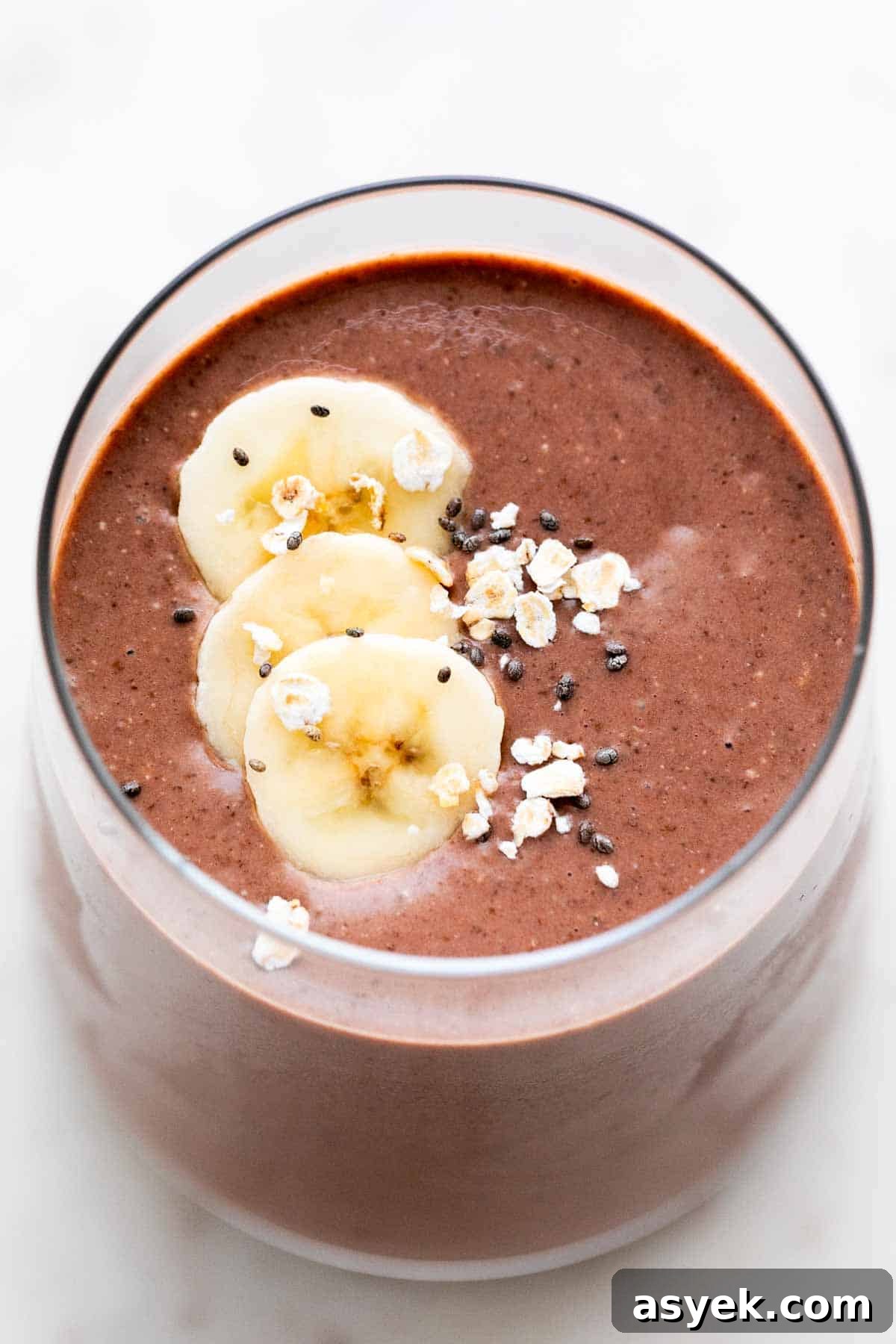 Glass of vegan protein shake garnished with banana, oats, and chia seeds.