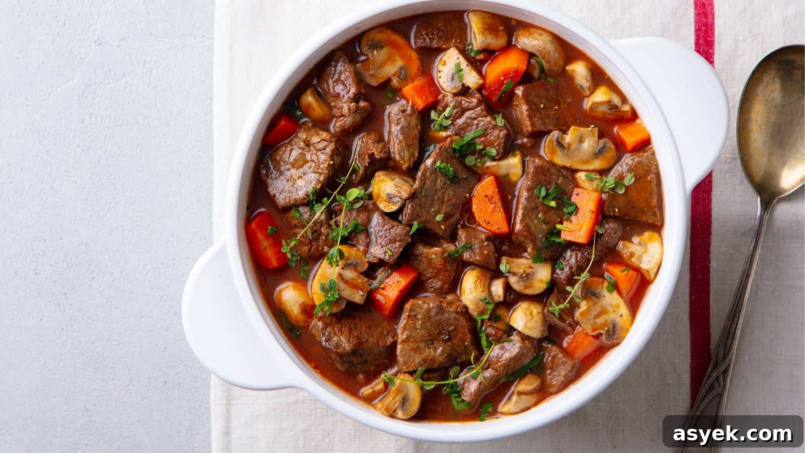 Beef stew in a white pot served with a spoon.