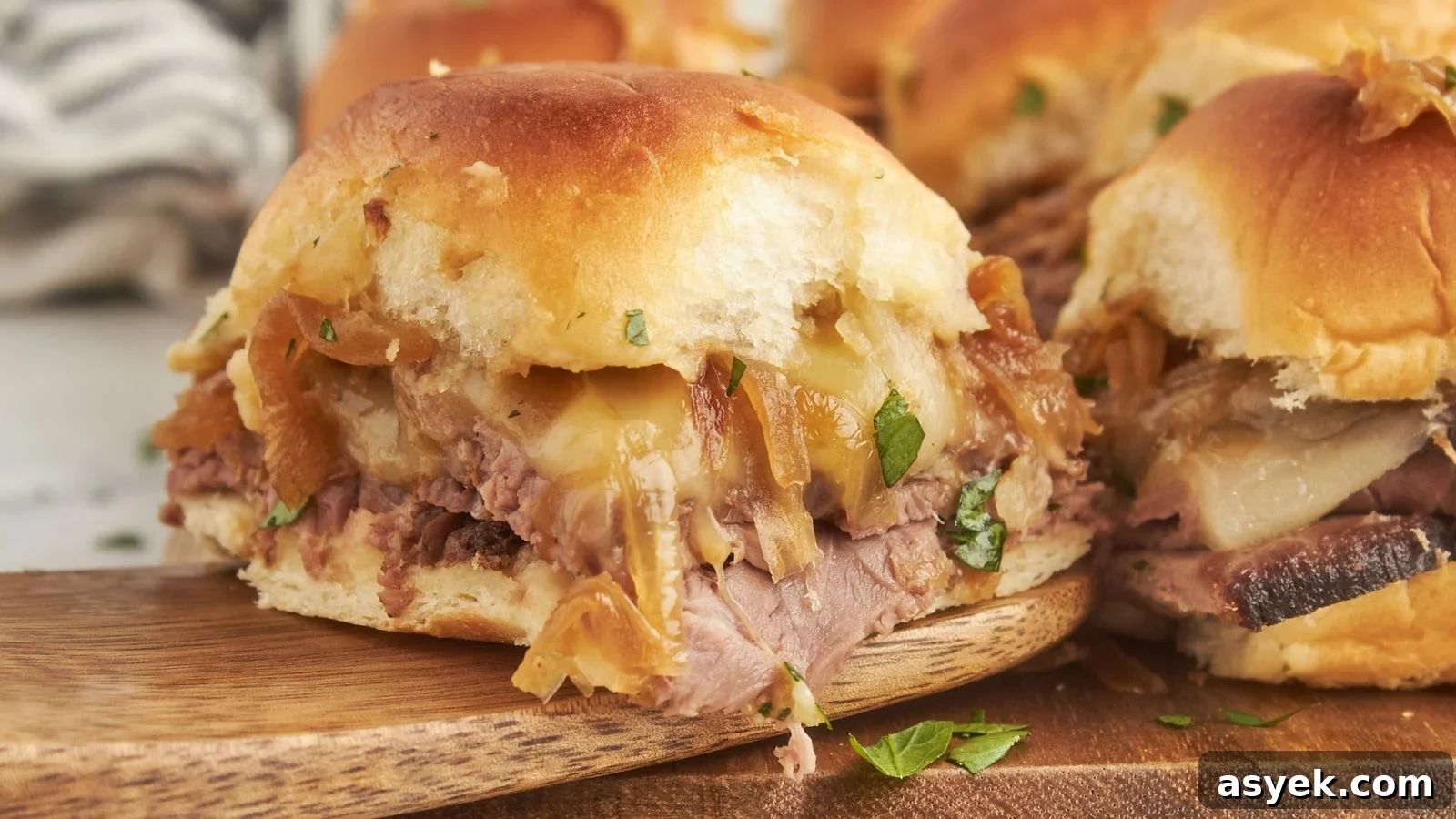 Small French dip sliders with melted cheese on toasted rolls served next to warm au jus.